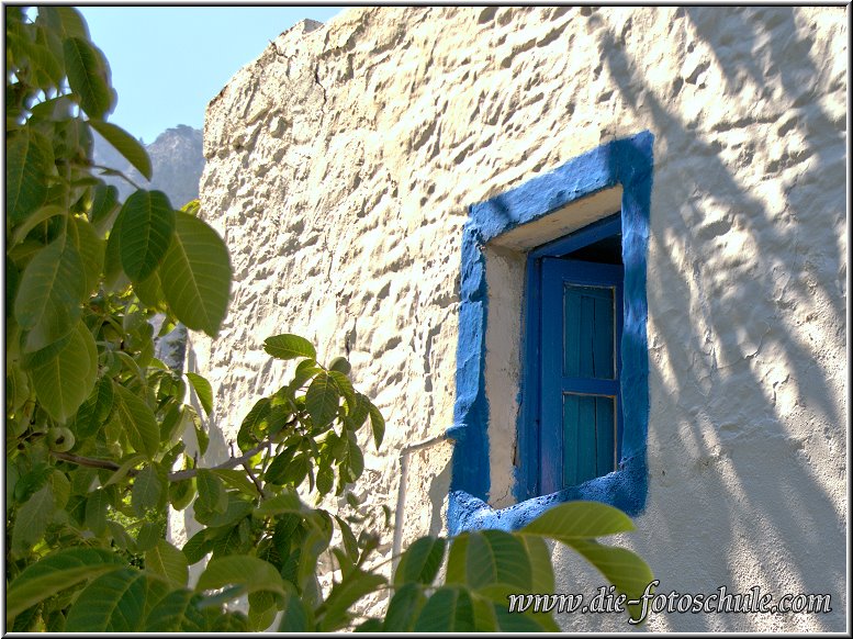 Zia_Tigaki_Fotoschule_006.jpg - Eine kleine weiß getünchte Kapelle mit kraftvoll blau abgesetzten Verzierungen, mitten auf einem gemütlichen Dorfplatz, auf dem ein großer Baum Schatten spendet, sorgt für eine unvergleichliche Stimmung.