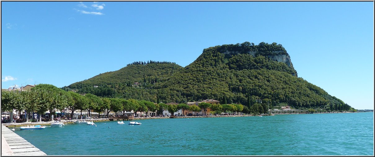 Garda_007.jpg - Auch Garda hat eine richtig schöne und ziemlich lange Uferpromenade und logischerweise auch zahllose Restaurants, Eisdielen und Cafes. Das Panorama mit der lang geschwungenen Promenade und dem Blick auf die grünen Berghügel und den irgendwie dunkler blau schimmernden See ist besonders eindrucksvoll. Hinzu kommt die sehr gepflegte und mit vielen Blumen und Anpflanzungen harmonisch wirkende Flaniermeile, breit und erhaben.