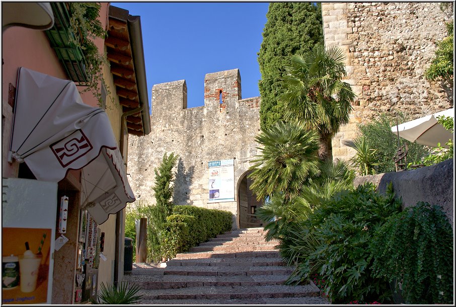 Malcesine_012.jpg - Über dem mittelalterlichen Ortskern mit vielen kleinen Plätzen (und Eisdielen), überwölbten Durchgängen und holprigen Pflasterwegen (die irgendwie alle zum alten Hafen runter führen) thront wieder mal, wie in anderen Orten rund um den See, eine mächtige Skaligerburg. Um sich die genauer anzuschauen, mußt Du allerdings 6 Euromünzen aus Deinem Geldschächtelchen holen.... Kurz vor dem Eingang zur Burg gibt es eine kleine Eisdiele, die richtig leckere selbstgemachte Eissorten anbietet. Vielleicht solltest Du Deine Taler besser hier investieren. Im Bild links zu sehen.