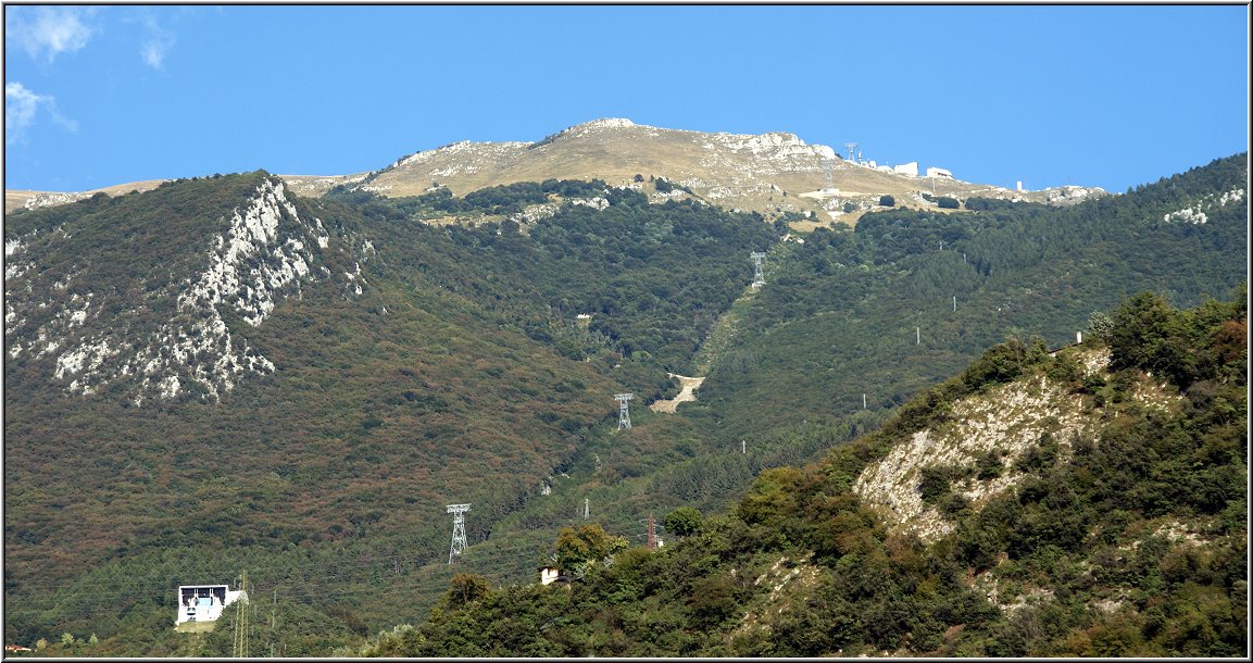 Malcesine_042.jpg - Und wie bereits erwähnt, Malcesine bringt Dich auf Wunsch ganz hoch hinaus:Von Malcesine fährt die Funivia Seilbahn zur 1760 Meter hoch gelegenen Bergstation auf einen Gipfel des Monte Baldos. Wenn Du das vorhast, solltest Du allerdings recht früh an der Talstation stehen, denn bei guter Fernsicht bildet sich hier auch in der Nebensaison eine meterlange Schlange (Wartezeit im Schnitt eine gute Stunde). Die Fahrt führt über eine Mittelstation, in der Du die Gondel wechselst (also aussteigen und einsteigen) steil hinauf. Der Ausblick schon in der Gondel ist grandios und einzigartig. Die obere Gondel nach der Mittelstation dreht sich während der Fahrt um 360 Grad. Ergatterst Du einen Fensterplatz, kannst Du das Panorama auf jeden Fall voll geniessen. Die oberen Gondeln (es sind zwei, eine hoch, eine runter) werden übrigens mit 77 Passagieren gefüllt, bevor es losgeht (nix für Leute, die den Atem des Nachbarn nicht mögen...). Unter der Talstation liegt ein Parkhaus, das Du über einen Kreisverkehr (wie sollte es auch anders sein) direkt von der Gardesana aus erreichen kannst. Die Parkgebühr beträgt für Seilbahnfahrer 4,50 EUR pro Tag, eine Fahrt hoch und runter mit der Seilbahn 18,-- EUR. Mountainbike-Fans können ihr Rad zu bestimmten Zeiten mitnehmen (gegen Gebühr), auch Paraglider müssen auf ihre Ausrüstung nicht verzichten.