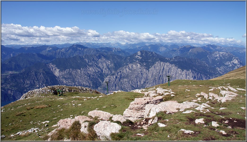 MonteBaldo_003.jpg - Oben auf dem Monte Baldo angekommen, bietet sich Dir ein sagenhafter Blick auf den in Bergketten eingebetteten Gardasee. Ich hatte richtig Glück, denn unser Monte Baldo Ausflug fiel auf den klarsten Tag unserer Reise und es gab eine Fernsicht bis weit in die Alpen hinein. Der See schimmerte klar und deutlich ganz weit unten, die Orte des Sees sahen aus wie kleine Sandkörnchen am Fuße der massiven Berge. Allerdings solltest Du bedenken, daß Du 1760 Meter über dem See bist. Wenn Du unten bei 27 Grad in die Gondel der Seilbahn steigst, wirst Du an der Bergstation von 12 Grad empfangen. Da war ich Flachlandtiroler nur unzureichend drauf vorbereitet und bekam mit meiner kurzen Hose recht frische Waden...