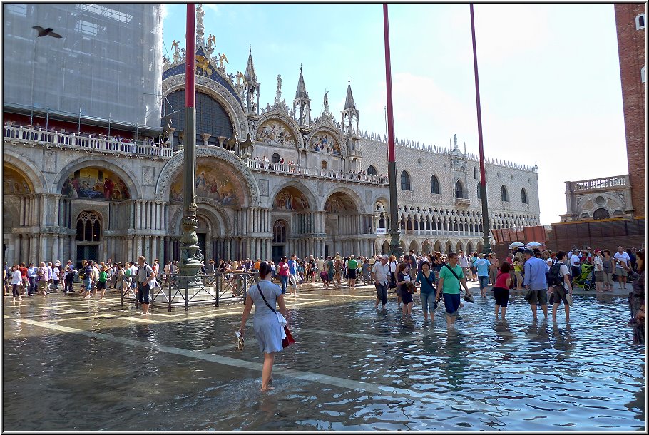 Venedig_Ralfonso_035.jpg - Dann endlich, der Markusplatz! Markuskirche, Dogenpalast, Markusturm, Uhrenturm...Die konnte ich erkennen, weil die ragten deutlich über die Massen auf dem Platz hinweg. Der Markusplatz selbst stand zum größten Teil unter Wasser; na ja, war ja eigentlich zu erwarten...Die Gewitter der Vortage haben wohl ganze Arbeit geleistet. Tausende liessen sich davon aber nicht beeindrucken und zogen ihre Socken und Schuhe aus und standen nun mitten drin in der Brühe. Der Versuchung konnte ich ohne große Überwindung aber widerstehen. Vor der Markuskirche standen gute 500 Menschen und warteten auf Einlass; barfuß in der Brühe. Ich könnte mich kringeln. Daß die meisten Fassaden des Markusplatzes eingerüstet waren und riesige Werbeplakate darauf klebten war schon schade. So kam ich zumindest in den Genuss, noch nie zuvor so riesengroße gesehene Plakate erleben zu können. Die Seufzerbrücke war förmlich eingepackt in Folie. Hier zeigt sich aber auch deutlich der fragliche Fokus, Venedigs Highlights rund um den Markusplatz mit großem Aufwand zu restaurieren und den "Rest" verfallen zu lassen. Die Menschen kommen nicht nach Venedig, um nur den Markusplatz zu sehen; auch wenn man anhand der Massen solches vermuten könnte. Wenn das Gesamtbild nicht mehr passt, wird aus der Perle Venedig schnell ein grauer schäbiger Stein Venedig. Und dagegen helfen dann auch keine automatischen Hochwasser-Schleusen am Eingang der Lagune. 